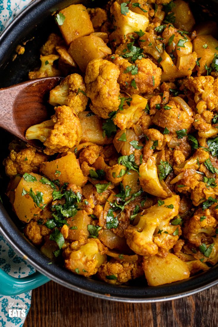 a skillet filled with cauliflower and potatoes on top of a wooden table