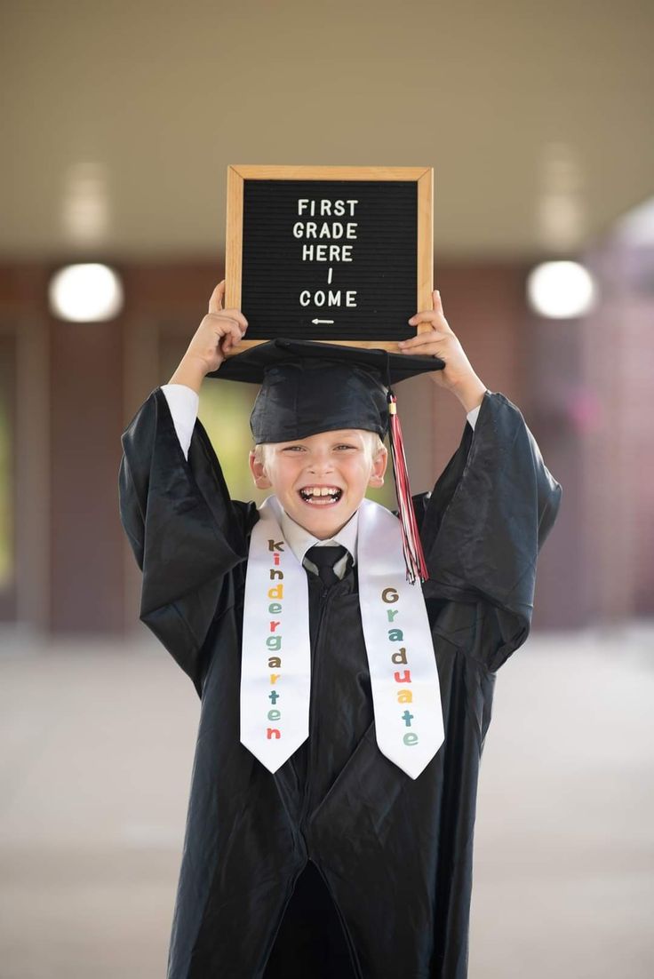 a young boy in graduation gown holding up a sign that says first grade here come