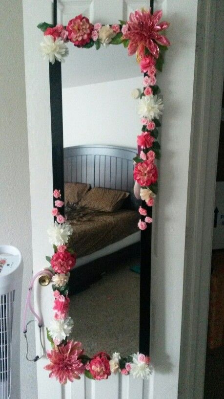 a mirror that has flowers on it in the shape of a flower frame with a bed in the background