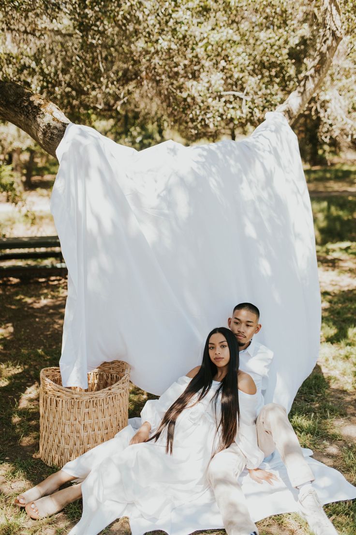 a man and woman sitting on the ground under a white sheet