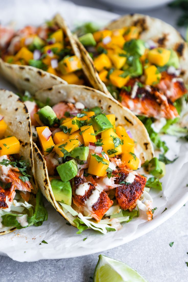 three fish tacos with mango salsa and avocado garnish on a white plate