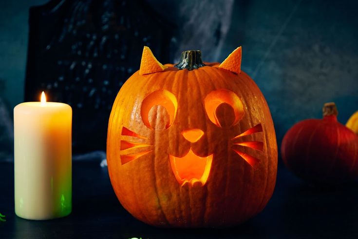 a carved pumpkin with a cat's face on it next to two lit candles