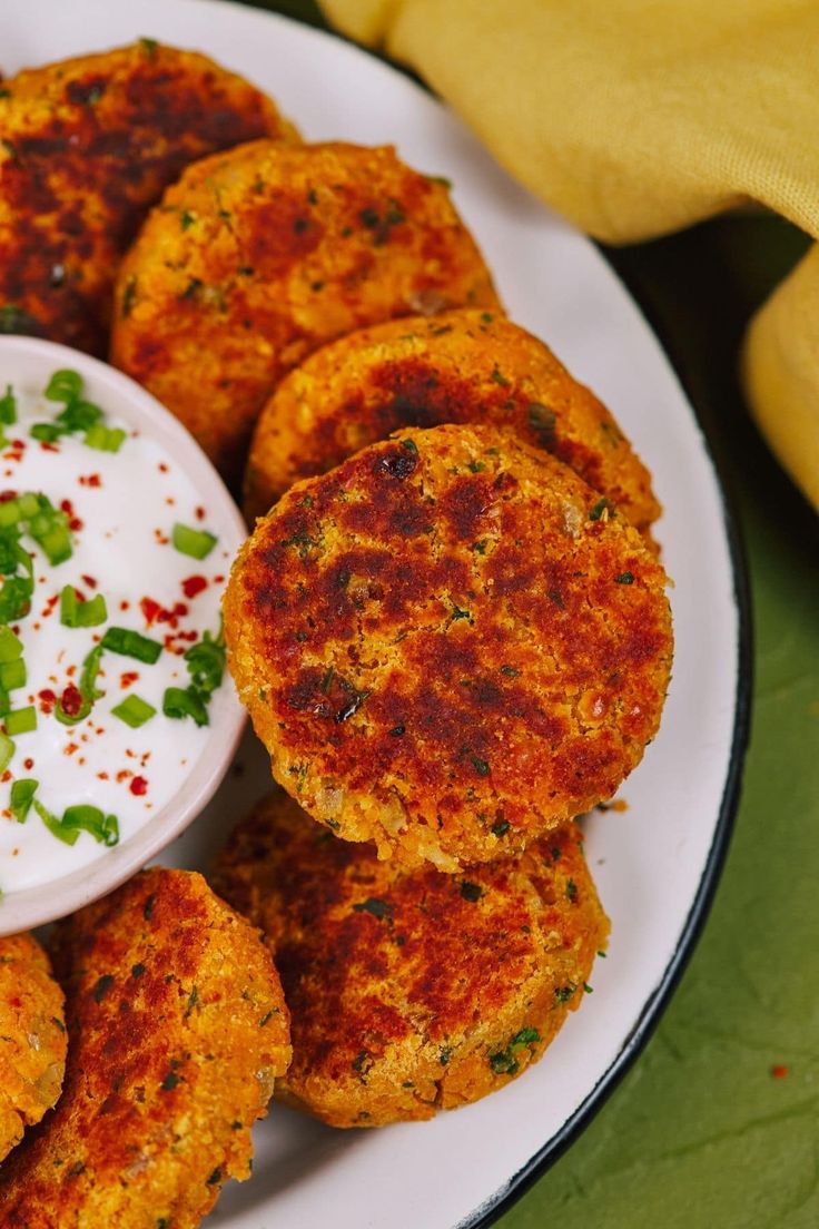 several crab cakes on a plate with sour cream and garnished green onions next to it