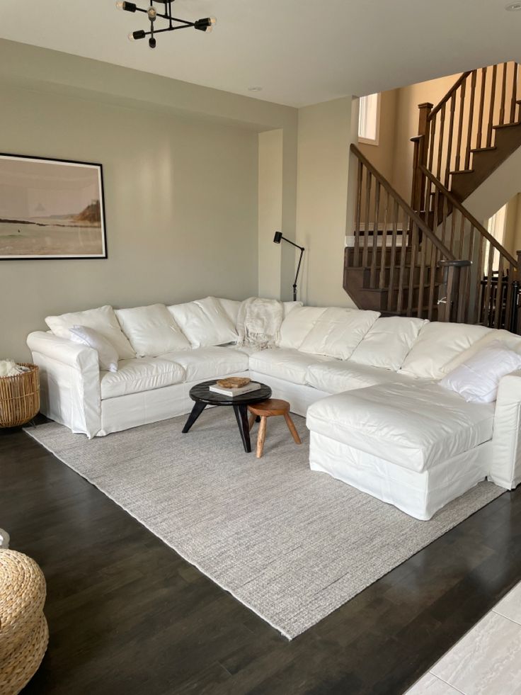 a large white sectional couch sitting in a living room next to a stair case and table