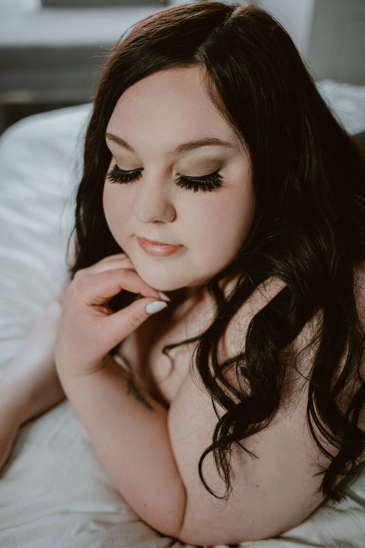 a naked woman laying on top of a bed with her hand under her chin and looking at the camera