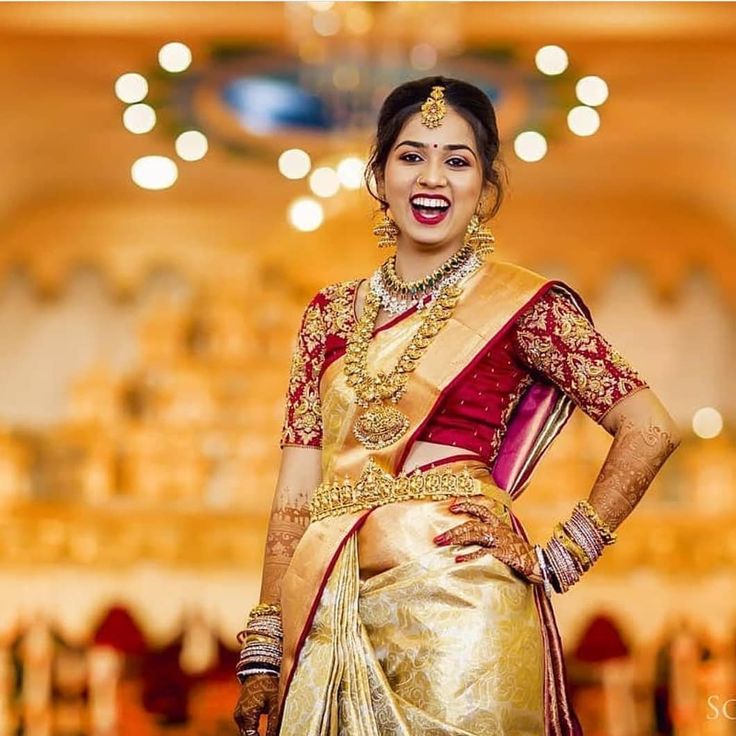 a woman in a gold and red bridal outfit with her hands on her hips