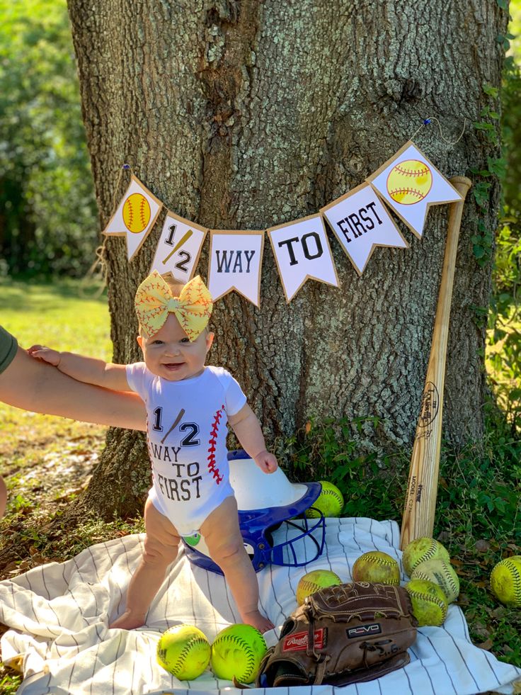 a baby is sitting on a blanket in front of a tree with baseballs and watermelons