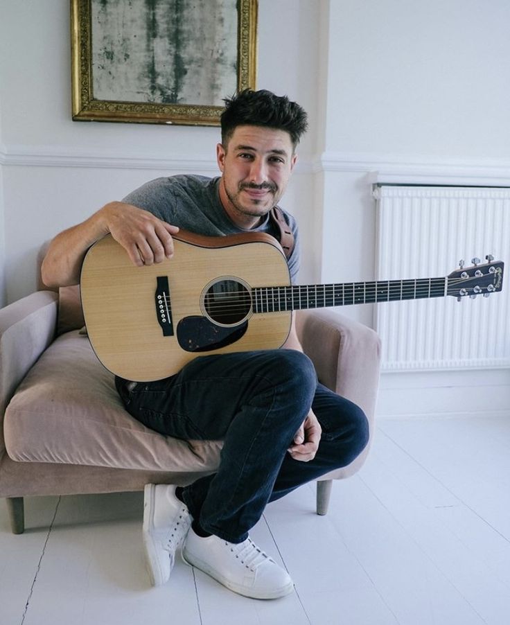 a man sitting on a chair holding a guitar in his hand and smiling at the camera