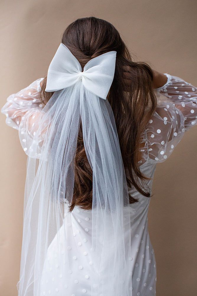 a woman wearing a veil with a white bow on her head and hair in the back