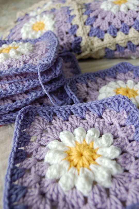 four crocheted squares with yellow and white flowers on them sitting on a table