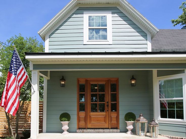 a blue house with an american flag on the front porch and two potted plants