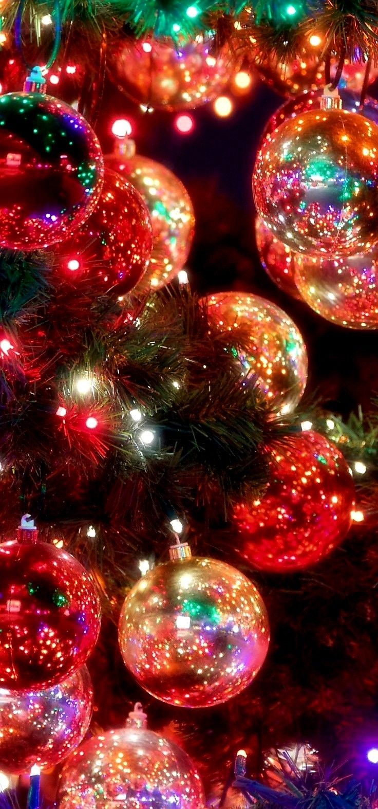 many shiny balls are hanging from a christmas tree with colorful lights on the branches and around them