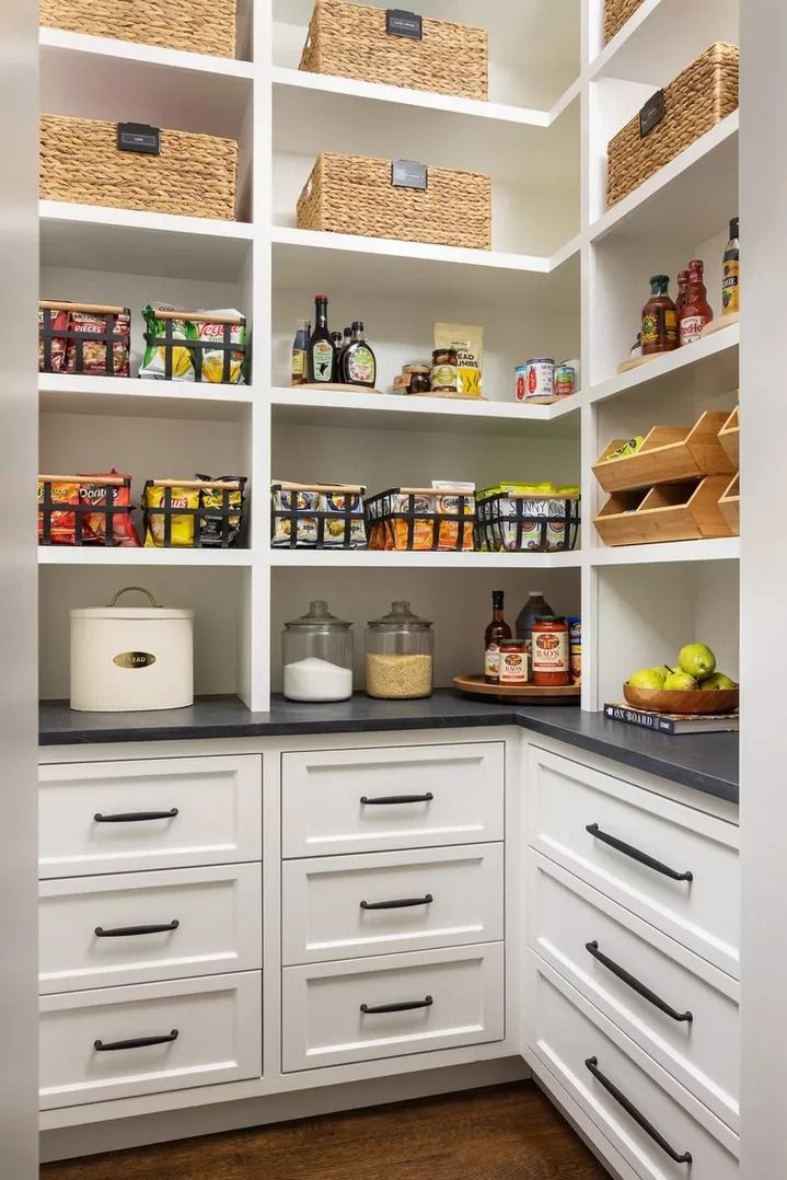 an organized pantry with white cabinets and black counter tops, wicker baskets on the shelves