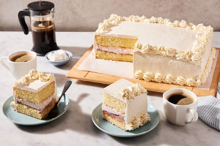 two slices of cake on plates next to cups and a coffee mug, with the rest of the cake in front of them