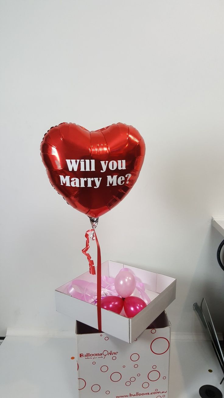 a red heart shaped balloon in a box with the words will you marry me?