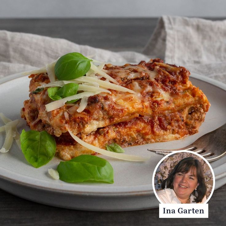 a white plate topped with lasagna covered in sauce and cheese next to a fork