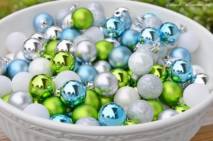 a white bowl filled with lots of green and blue christmas ornament ornaments on top of a wooden table