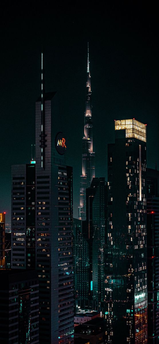 the city skyline is lit up at night with skyscrapers in the foreground and other tall buildings