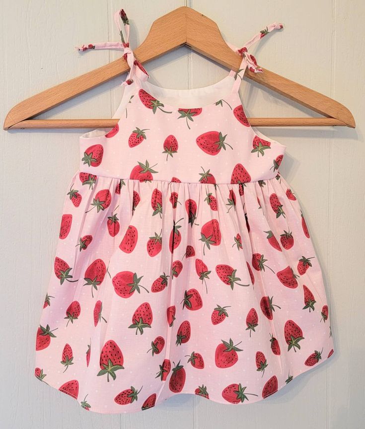 This fun and summery strawberry sundress with matching bloomers for babies and toddlers features a full skirt and shoulder ties that tie into a bow. The bodice is lined with soft cotton and there are no exposed seams on the bodice sides for a more comfortable fit. Fabrics are woven cotton and are machine washable in cool water with like colors and can be machine dried on a low setting. This dress would be great to wear to a Strawberry themed party or event or for everyday wear and play. Sizing i Cute Summer Bubble Romper For Garden Party, Cute Sundress With Tie Straps For Garden Party, Cotton Bubble Romper For Spring Garden Party, Sweet Pink Bubble Romper For Summer, Spring Garden Party Cotton Bubble Romper, Cute Summer Dresses With Tie Back, Playful Summer Dress With Tie Straps, Sweet Summer Beach Dresses, Summer Cotton Sundress For Babies