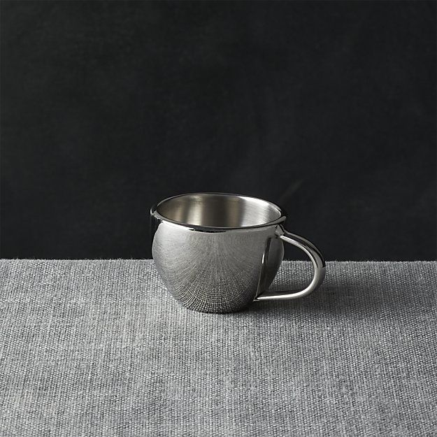 a silver cup sitting on top of a table next to a gray cloth covered floor