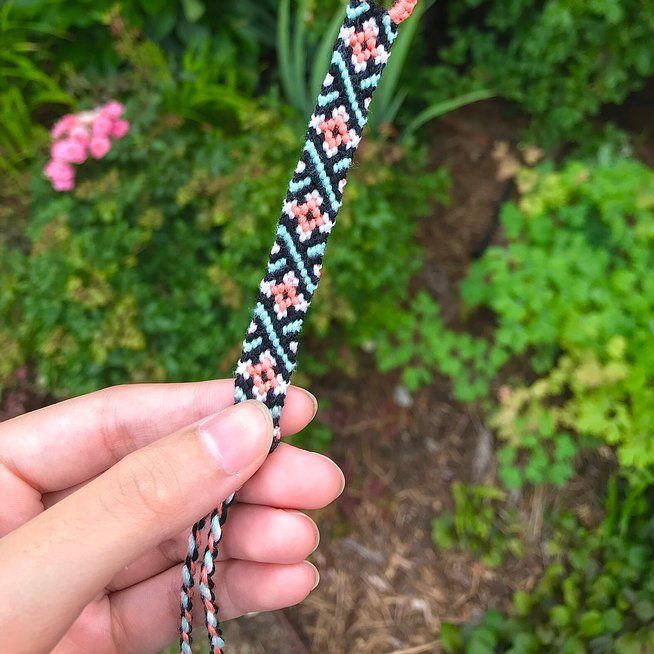 a hand holding a black and white braided cord with pink flowers on the end