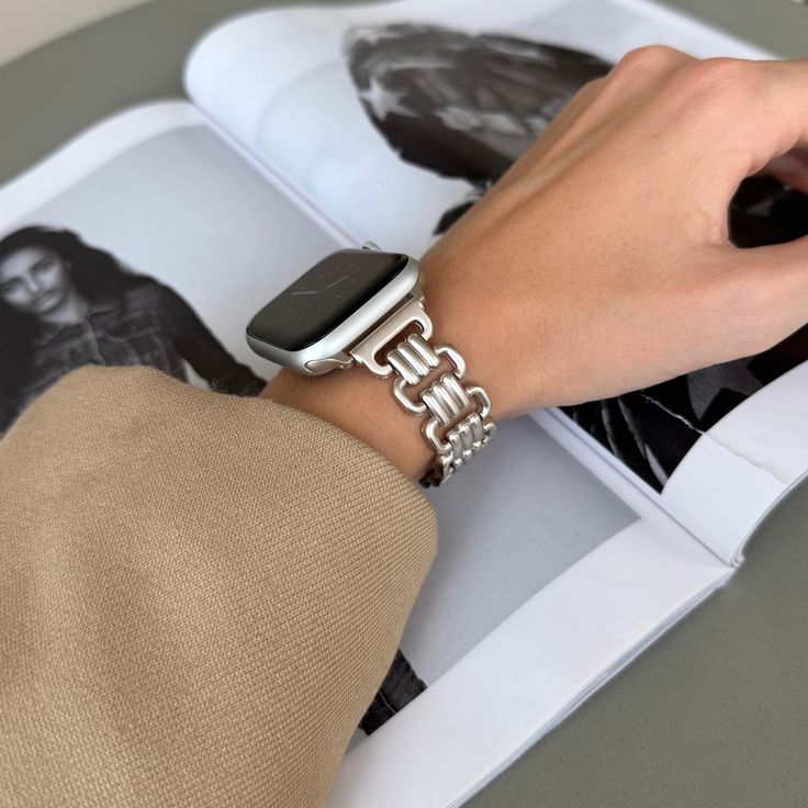 a person wearing an apple watch on their wrist with a book in the back ground