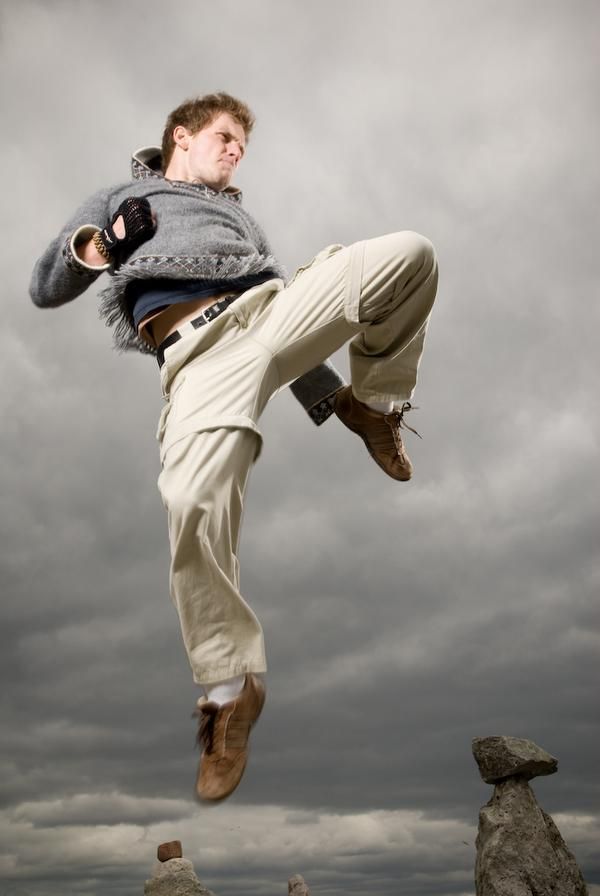 a man is jumping in the air with his feet up on some rocks and cloudy skies