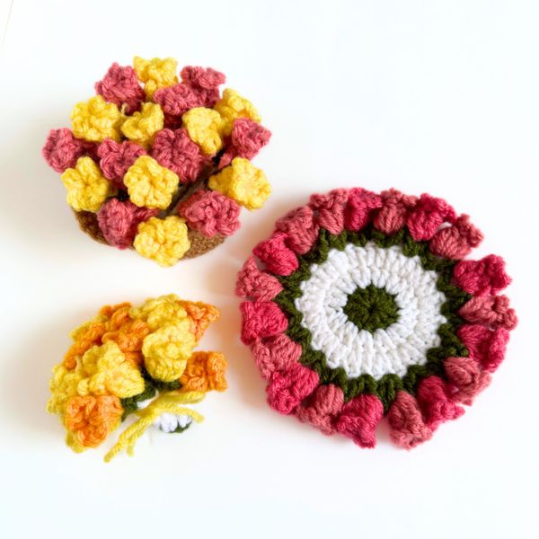 three crocheted bowls with flowers in them on a white surface, one is yellow and the other is red