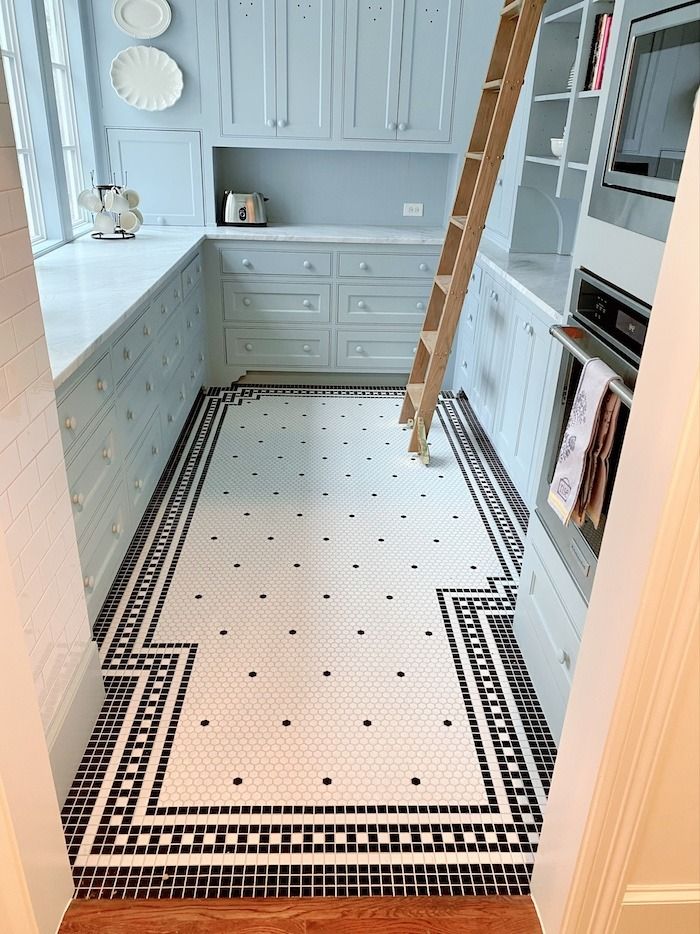 a kitchen with white cabinets and black and white floor tiles on the floor is a ladder in the middle of the room