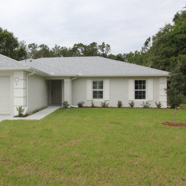 a white house sitting in the middle of a lush green field with trees around it