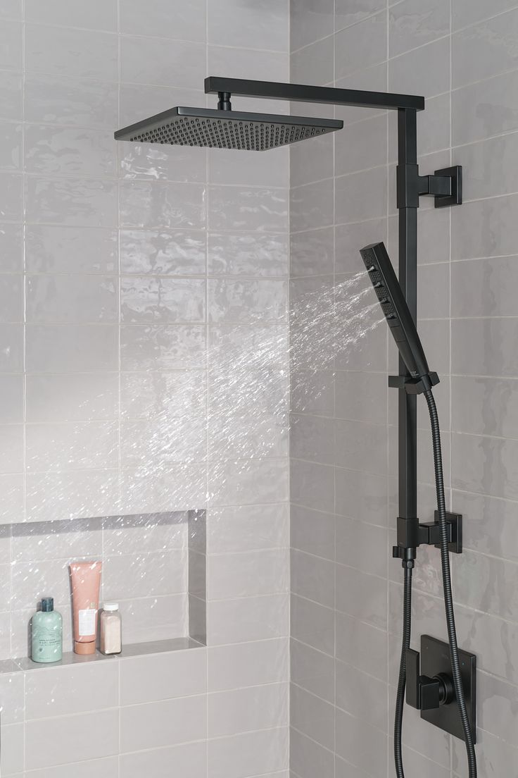 the shower head is open and there are soaps on the shelf next to it