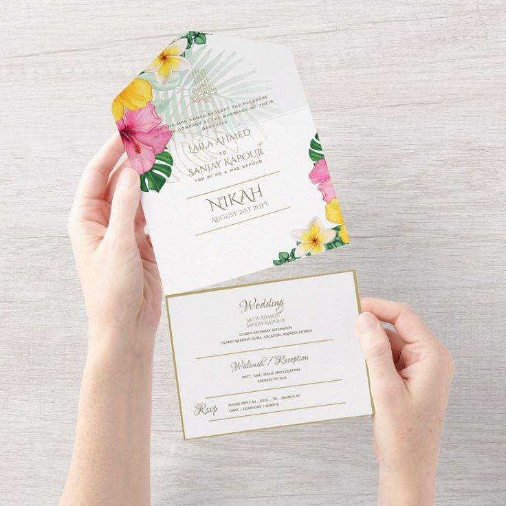 a person holding up a wedding card with flowers on the front and bottom, while another person holds it in their hand