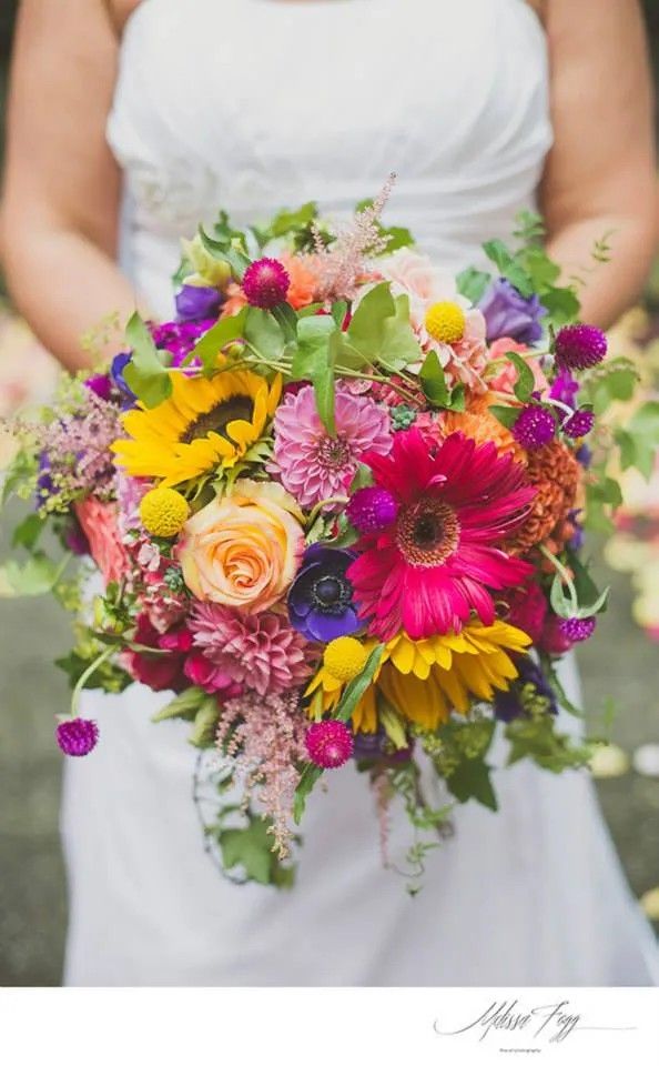 a woman holding a bouquet of flowers in her hands and wearing a white dress with red, orange, yellow and purple flowers