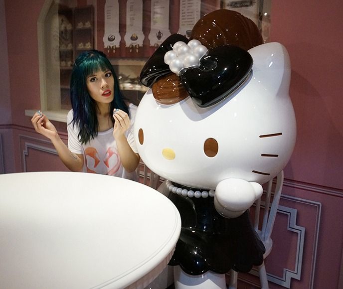 a woman standing in front of a hello kitty statue next to a white table and chair