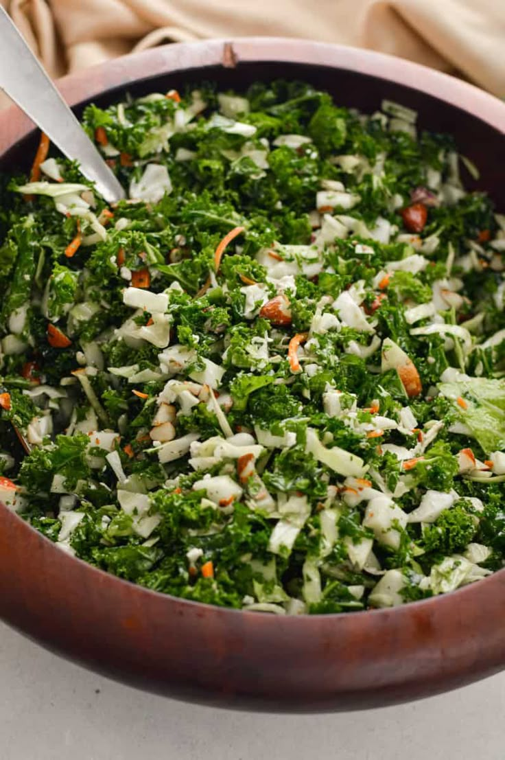 a wooden bowl filled with lots of green food next to a knife and fork on top of a table