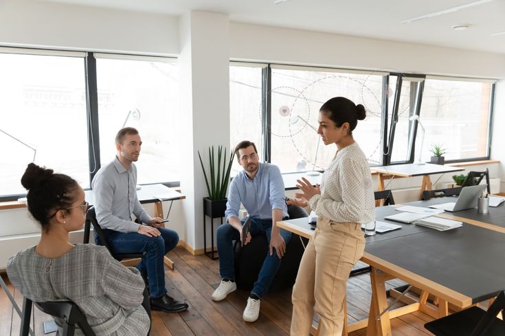 a group of people sitting around a table talking to each other in front of large windows