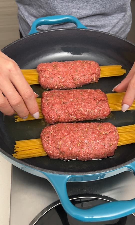 two sausage patties being cooked in a frying pan on the stove top with yellow noodles