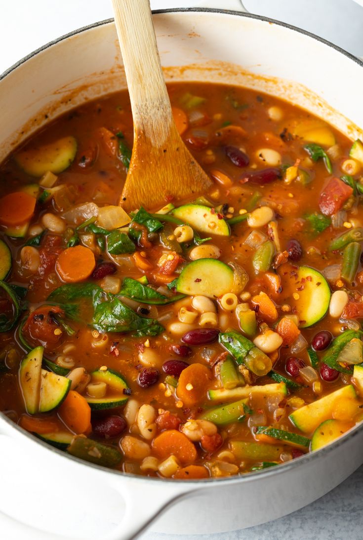 a pot full of vegetable soup with a wooden spoon