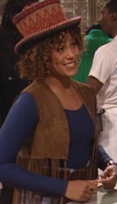 a woman wearing a hat standing in front of a counter with other people around her