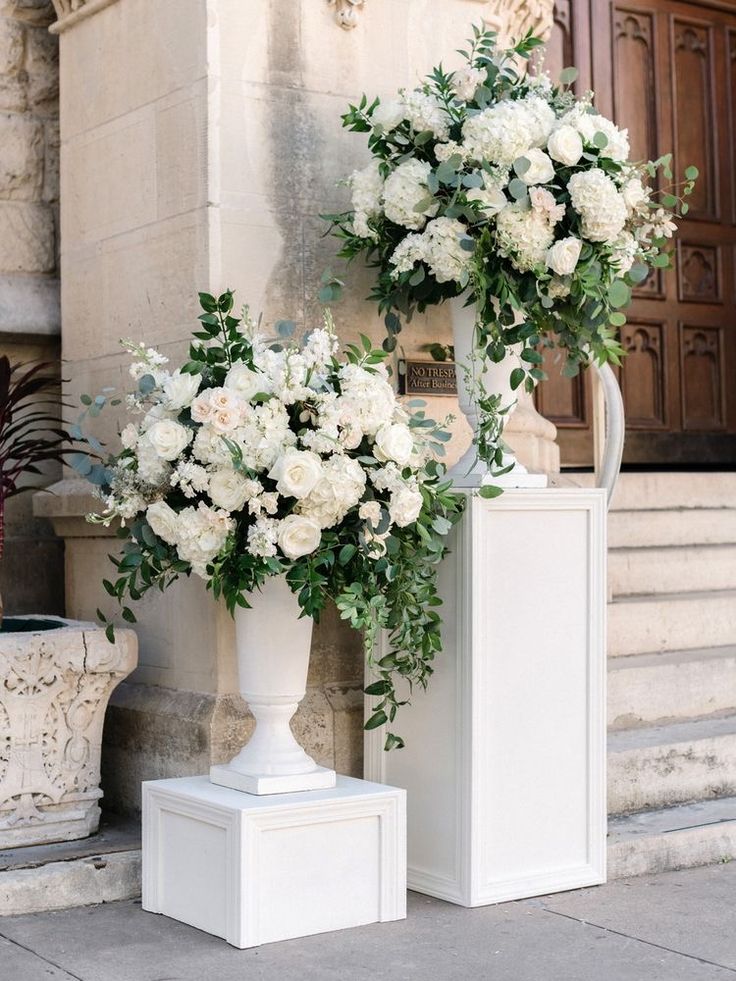 two white vases filled with flowers sitting on the side of a building