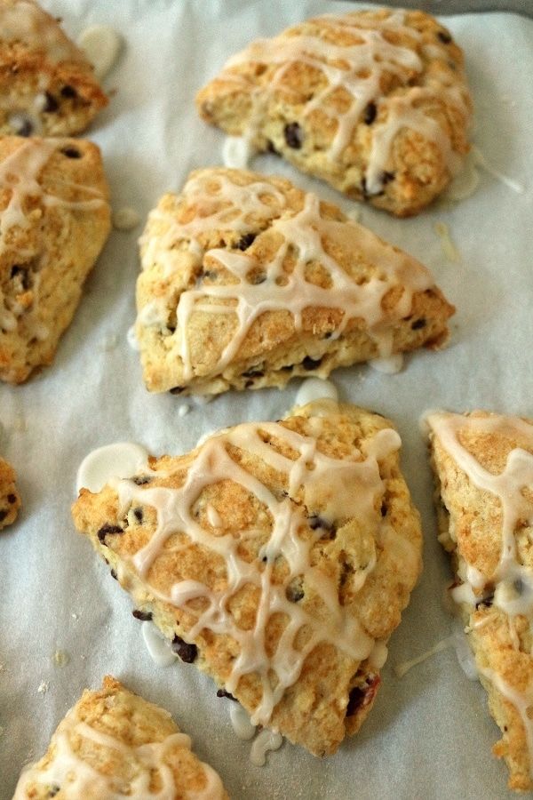 several scones with icing and raisins on a piece of parchment paper