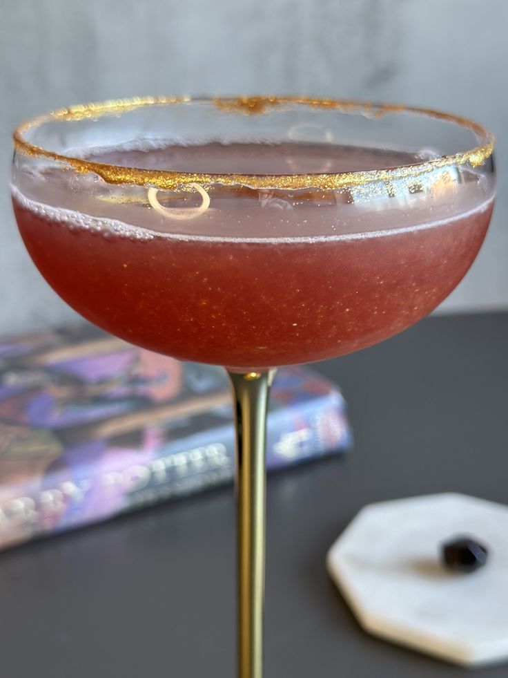 a close up of a wine glass on a table with a book in the background