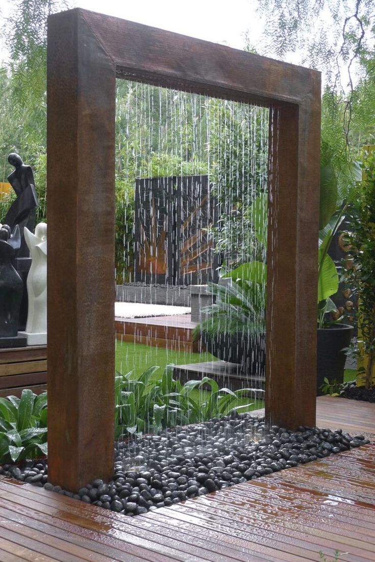 an outdoor fountain in the middle of a wooden deck with rocks and plants around it