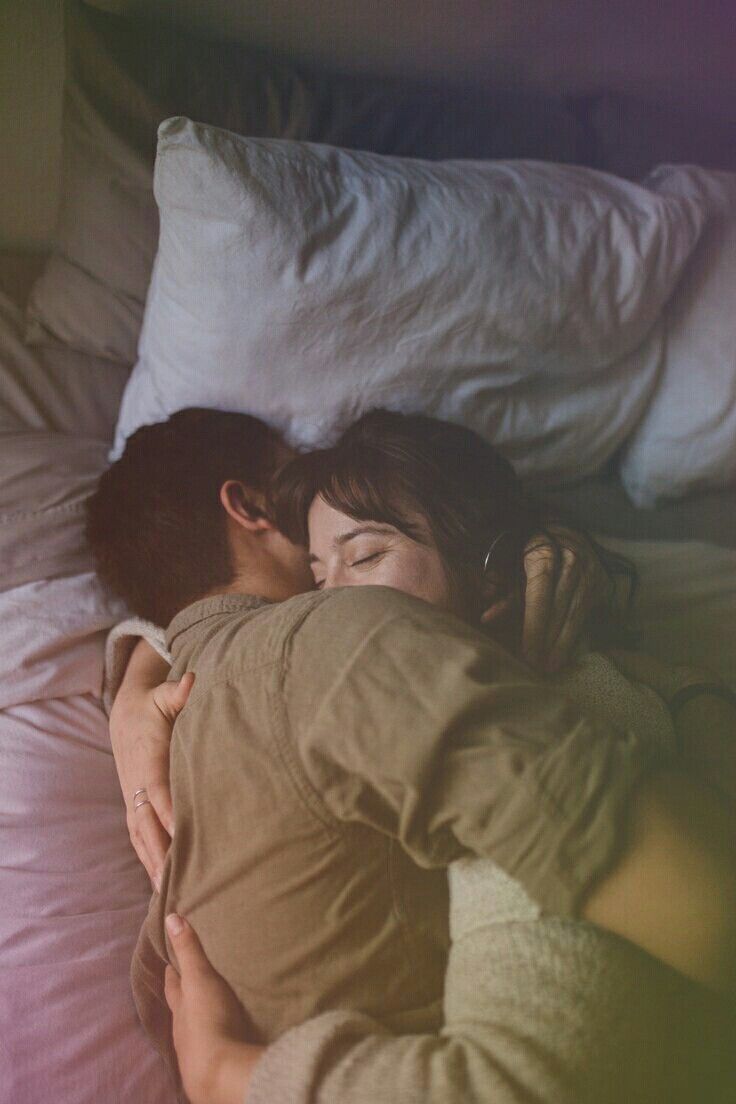 a man and woman laying in bed with their head on each other's shoulders