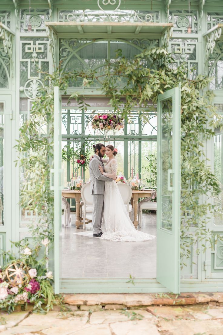 a bride and groom standing in front of an open door with greenery on it