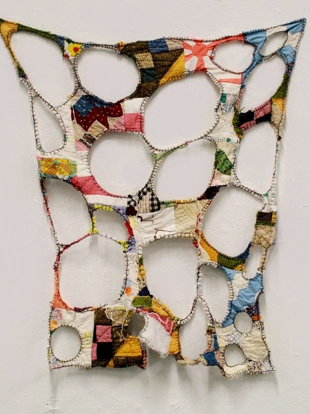 a piece of art made out of different types of fabric and buttons on a white wall