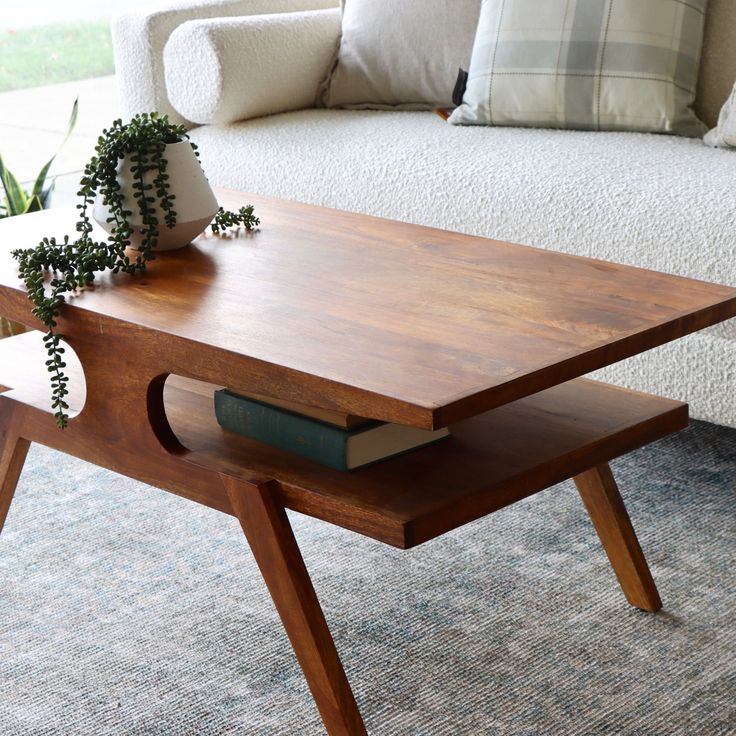 a wooden table with a book on it in front of a white couch and pillows