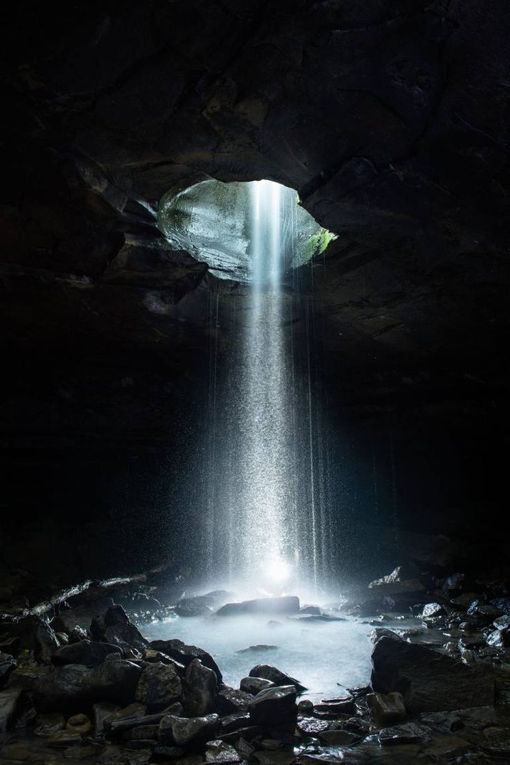 the light is shining down from the cave into the water and it appears to be coming out