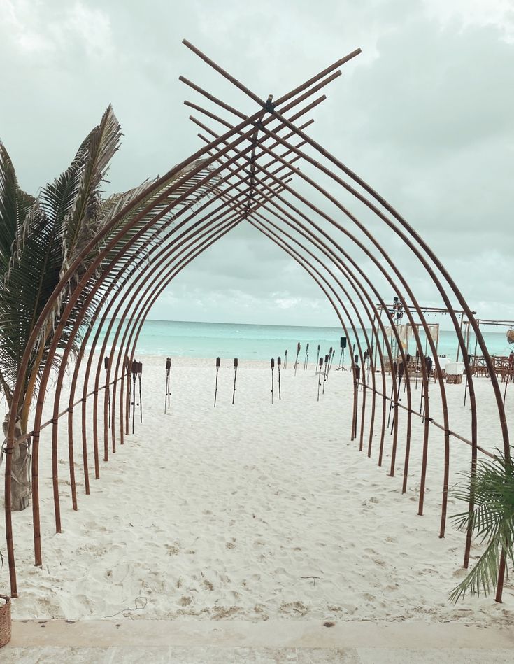 an archway on the beach with palm trees and people in the water behind it,