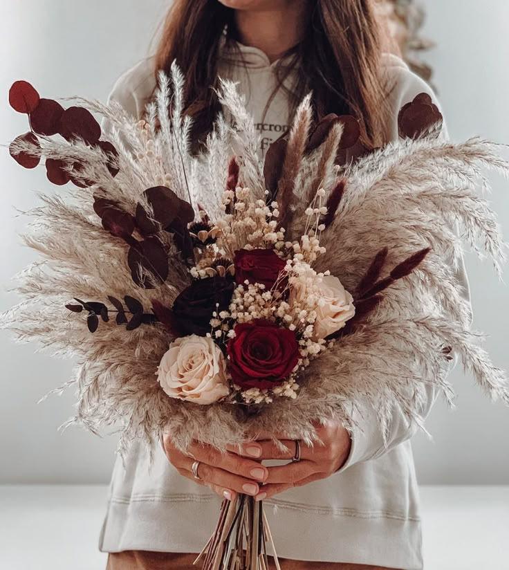 a woman holding a bouquet of dried flowers and feathers in front of her face while wearing a white shirt